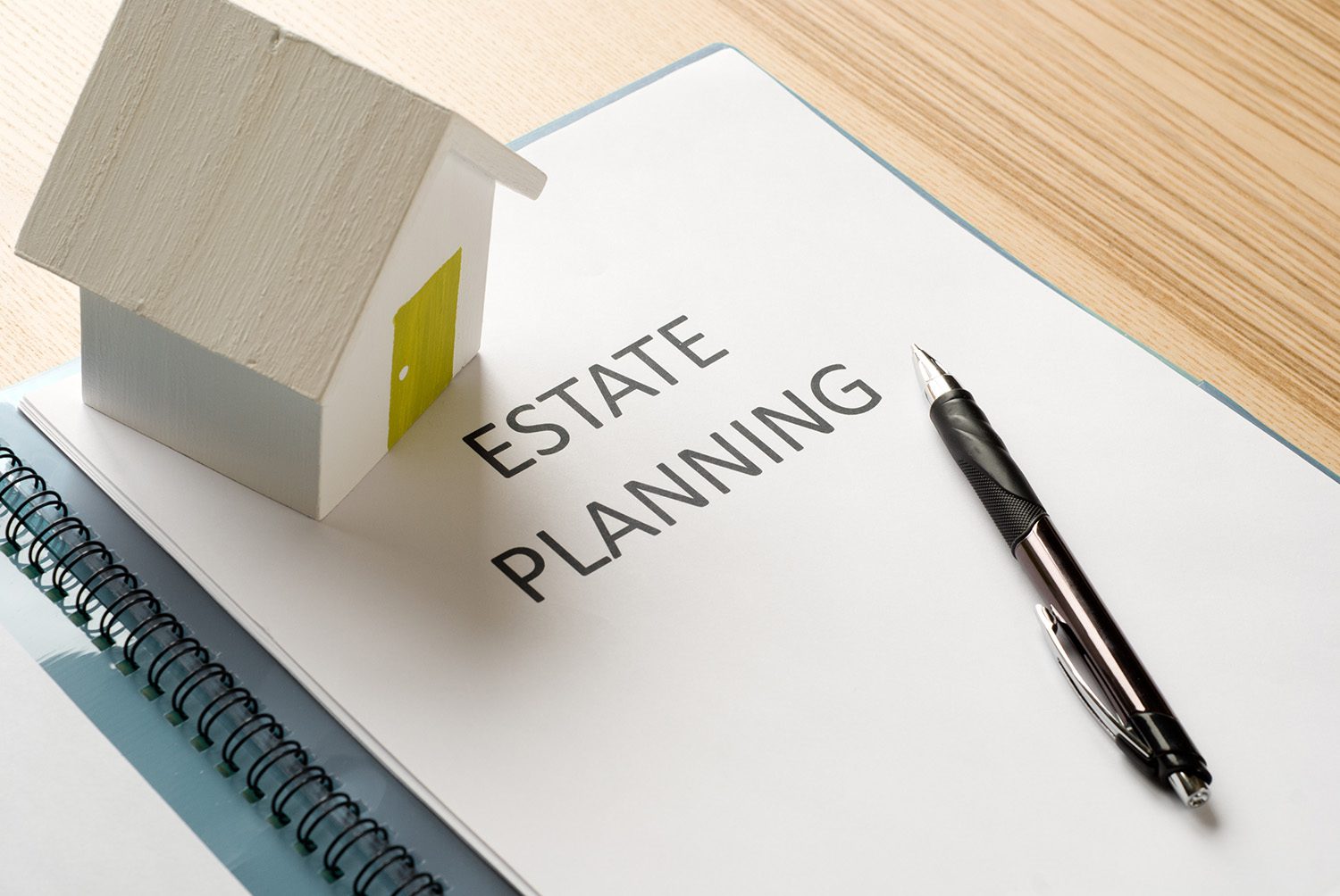A piece of paper that says "estate planning" with a pen and a small house figure on either side of the word.
